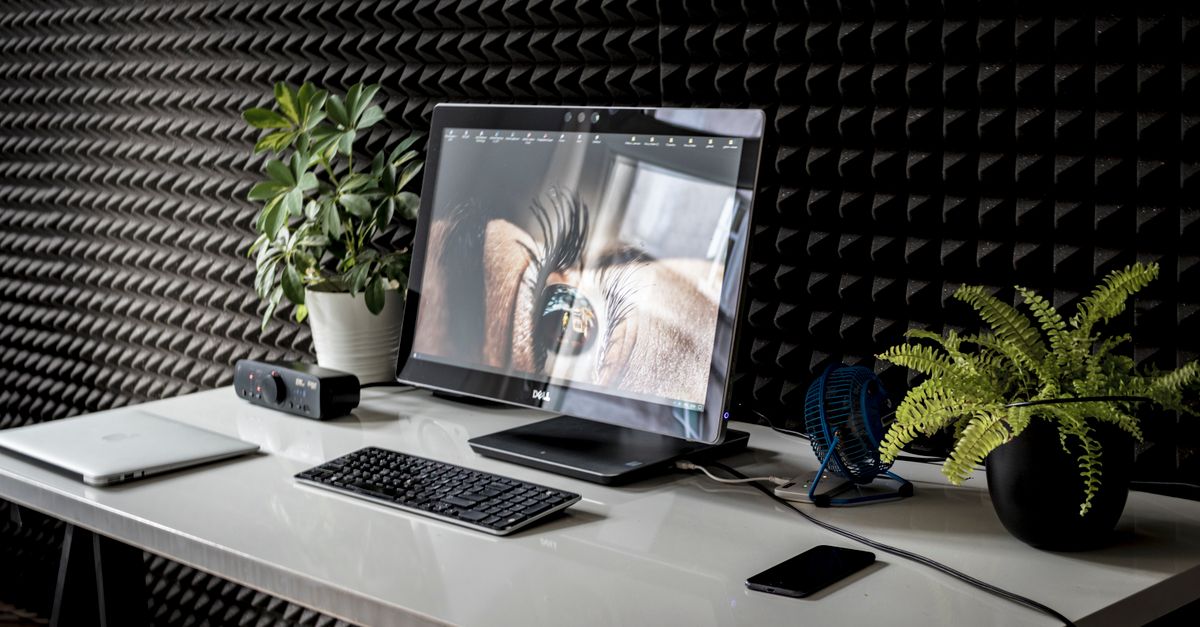 A contemporary desk setup with a desktop computer, keyboard, and green plants in a modern office.